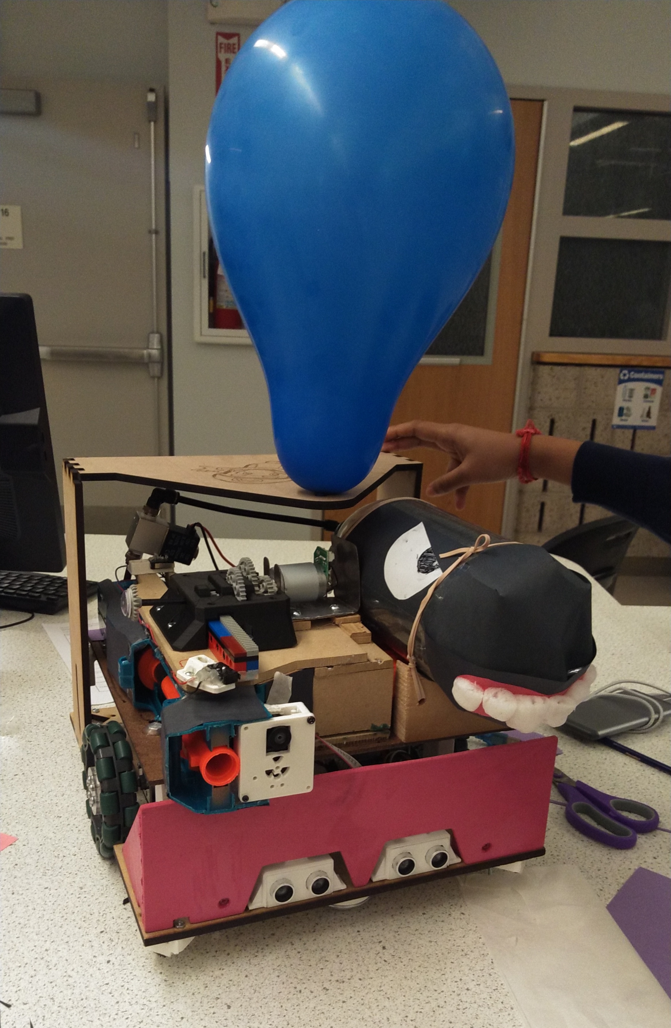 a robot sitting on a table. It has a balloon attached to its top.